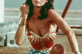 American actor Lynda Carter kneels on the ground and bears her forearm in a still from the television series Wonder Woman