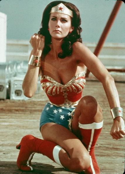 American actor Lynda Carter kneels on the ground and bears her forearm in a still from the television series Wonder Woman