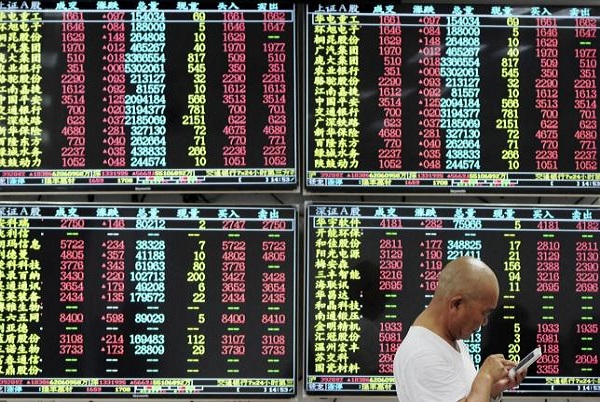  An investor looks at his mobile phone in front of electronic screens showing stock information at a brokerage house in China
