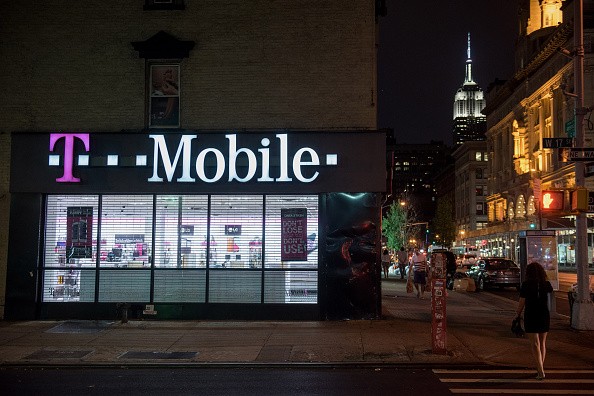 Pedestrians walk past a T-Mobile US Inc. store at night as the Empire State building stands in New York, U.S., on Sunday, July 26, 2015. T-Mobile US Inc. is scheduled to release earnings figures on July 30.