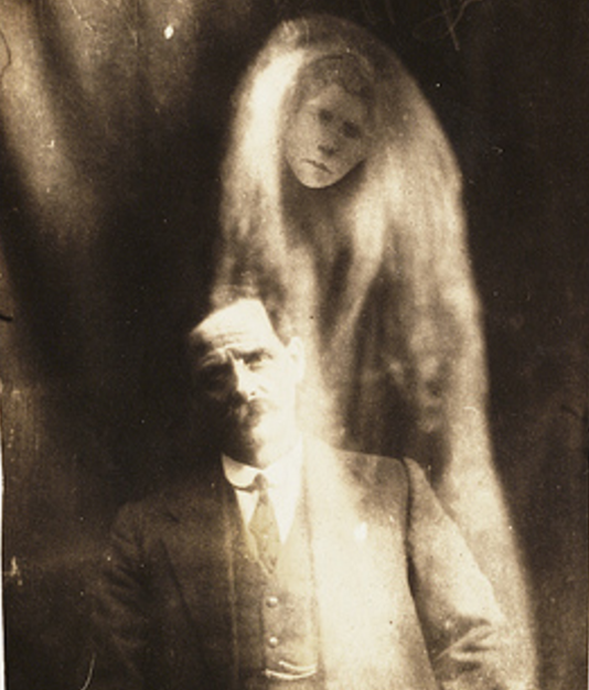 A woman's face appears in 'misty' drapes around the man. He was said to have been asked to sit for a photograph by a voice heard at a seance held on 6 May 1923.