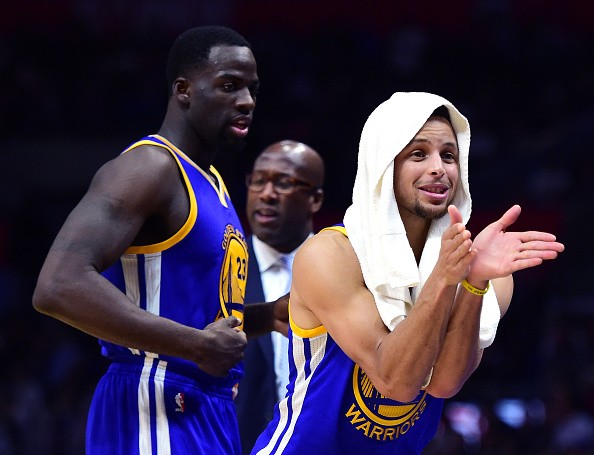 Stephen Curry #30 of the Golden State Warriors jokes on the sidelines in front of Draymond Green #23 and Mike Brown during a 115-98 Warriors win over the LA Clippers at Staples Center on December 7, 2016 in Los Angeles, California. 